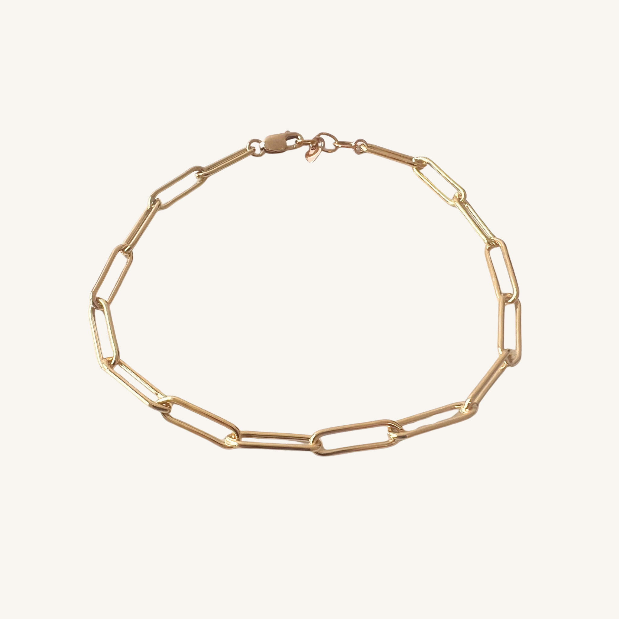 A gold paperclip chain bracelet with a lobster clasp, displayed on a clean off-white background.