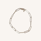 A silver paperclip chain bracelet, displayed on a light cream background.