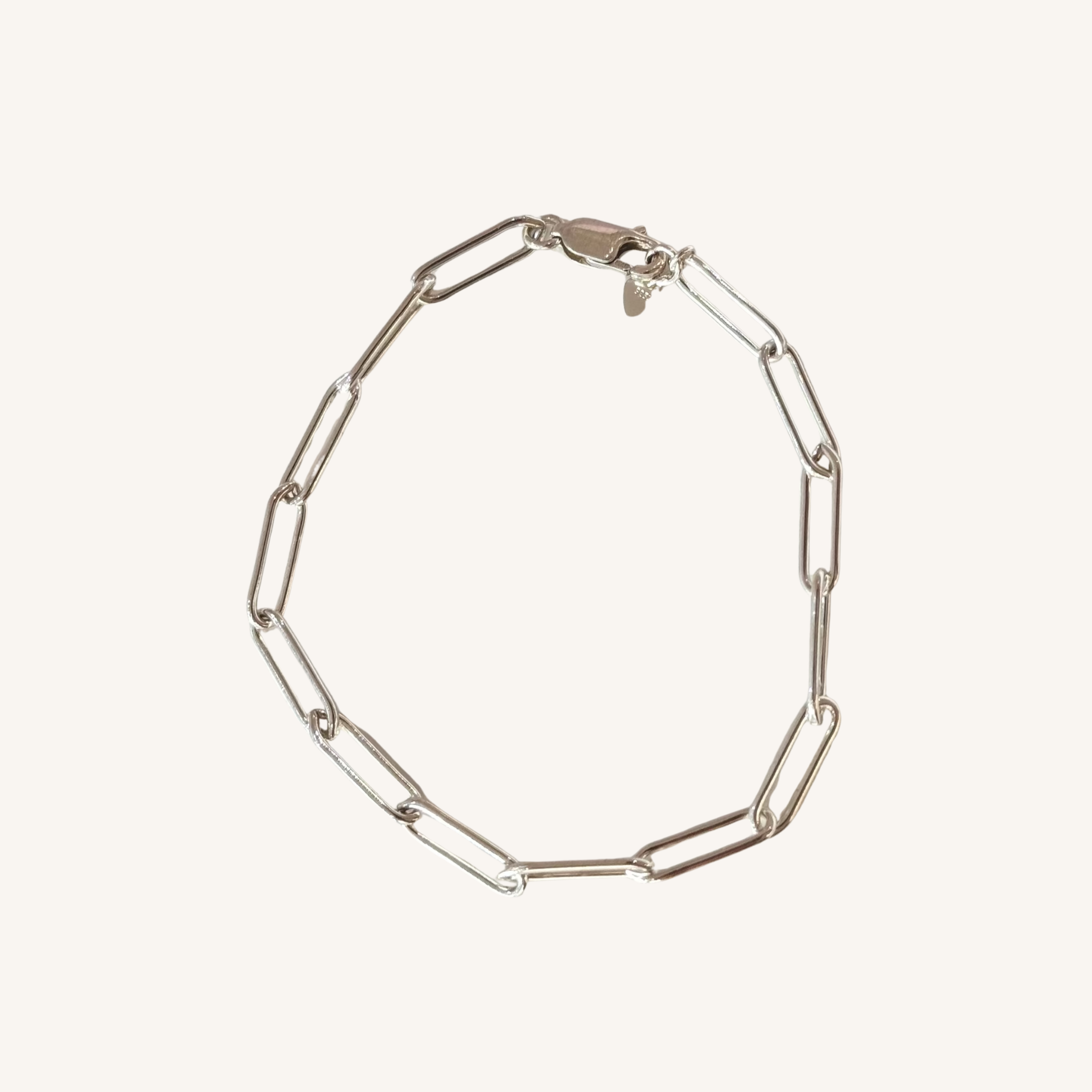 A silver paperclip chain bracelet, displayed on a light cream background.