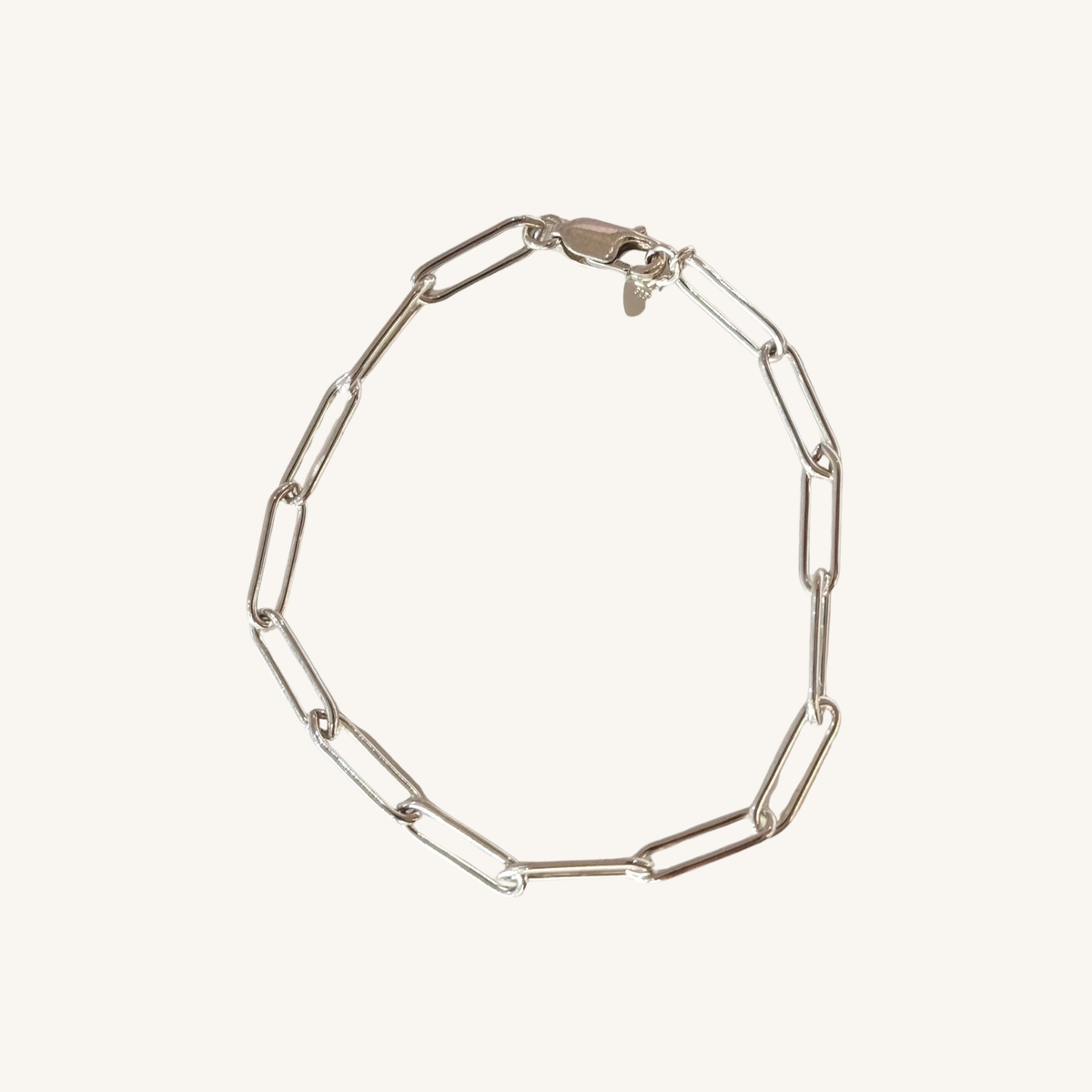 A silver paperclip chain bracelet, displayed on a light cream background.