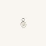 A small round diamond charm in silver, centered on a light cream background.