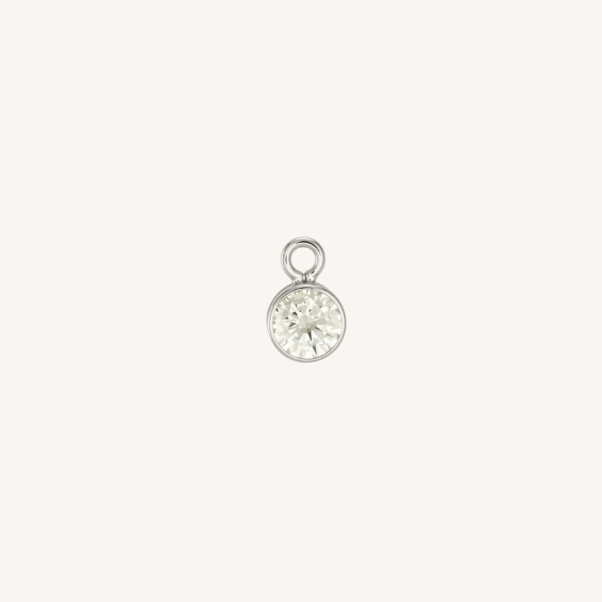 A small round diamond charm in silver, centered on a light cream background.