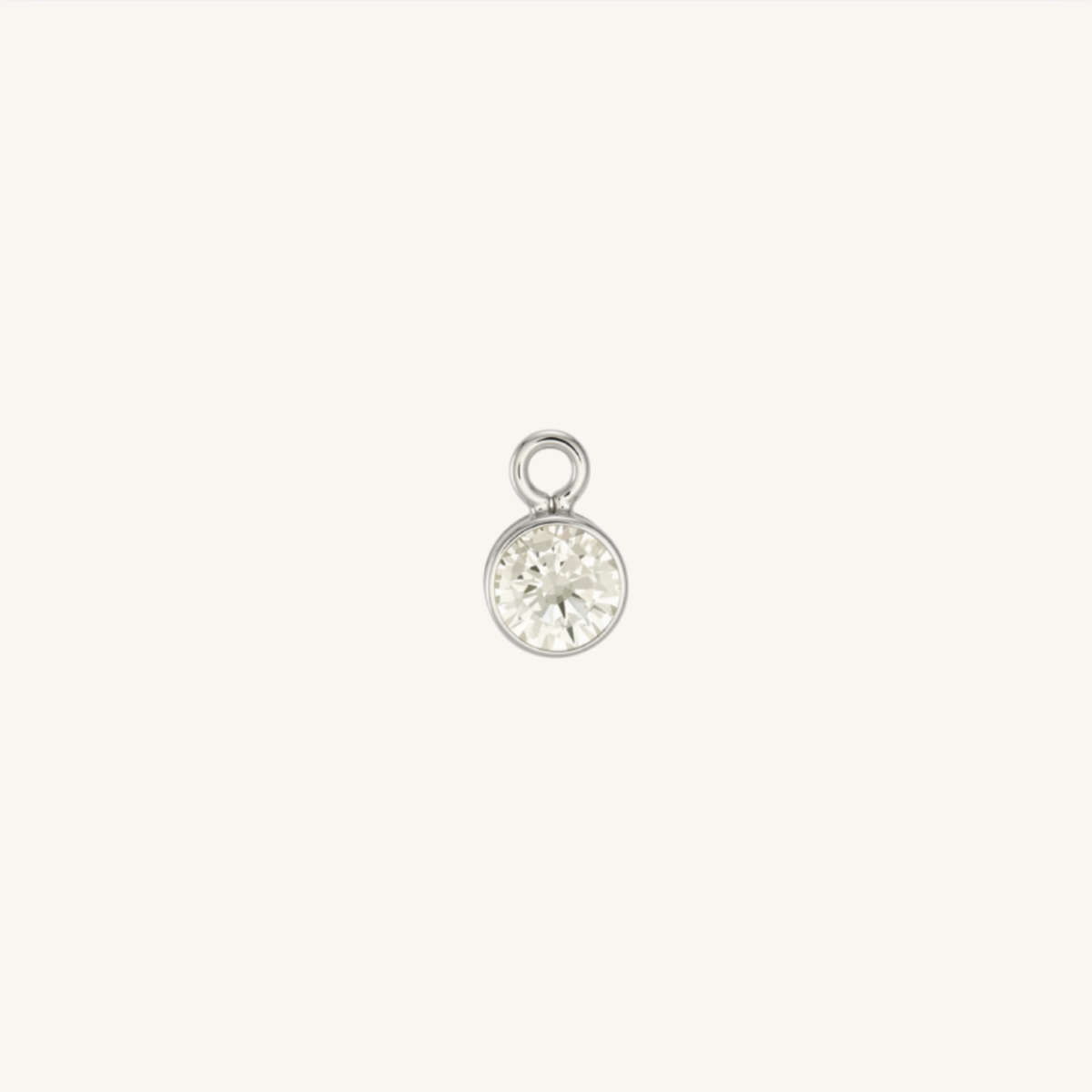 A small round diamond charm in silver, centered on a light cream background.