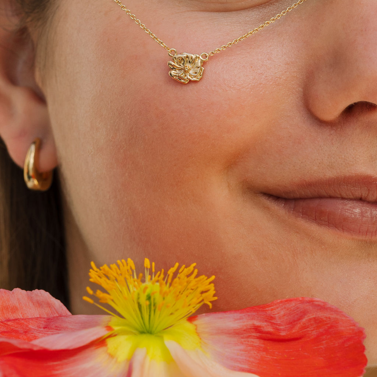 Close-up of a woman's face with gold jewelry and a red flower.