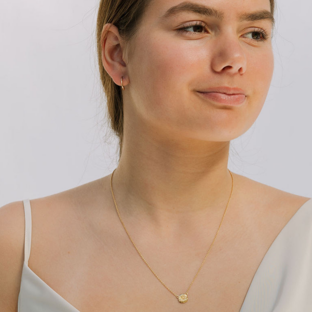 Woman wearing a gold necklace against a plain background