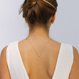 Woman wearing a gold necklace with a white top against a light gray background