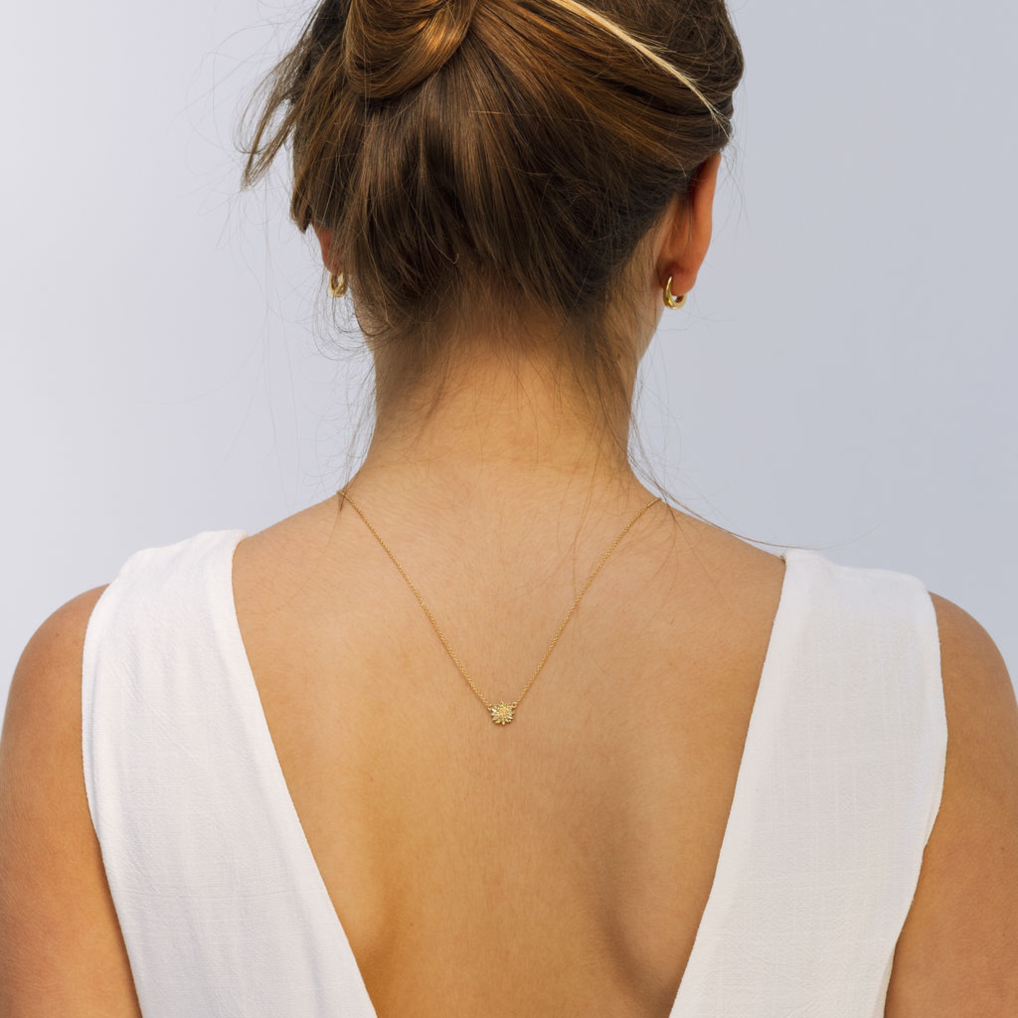Woman wearing a gold necklace with a white top against a light gray background