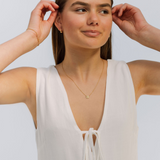 Woman wearing a white sleeveless top and gold necklace against a light background