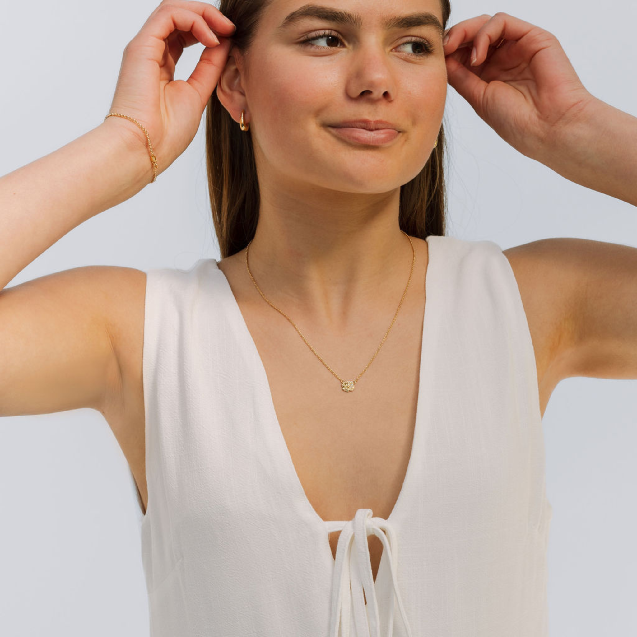 Woman wearing a white sleeveless top and gold necklace against a light background