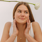 Woman with hands on face against a light background with a white flower