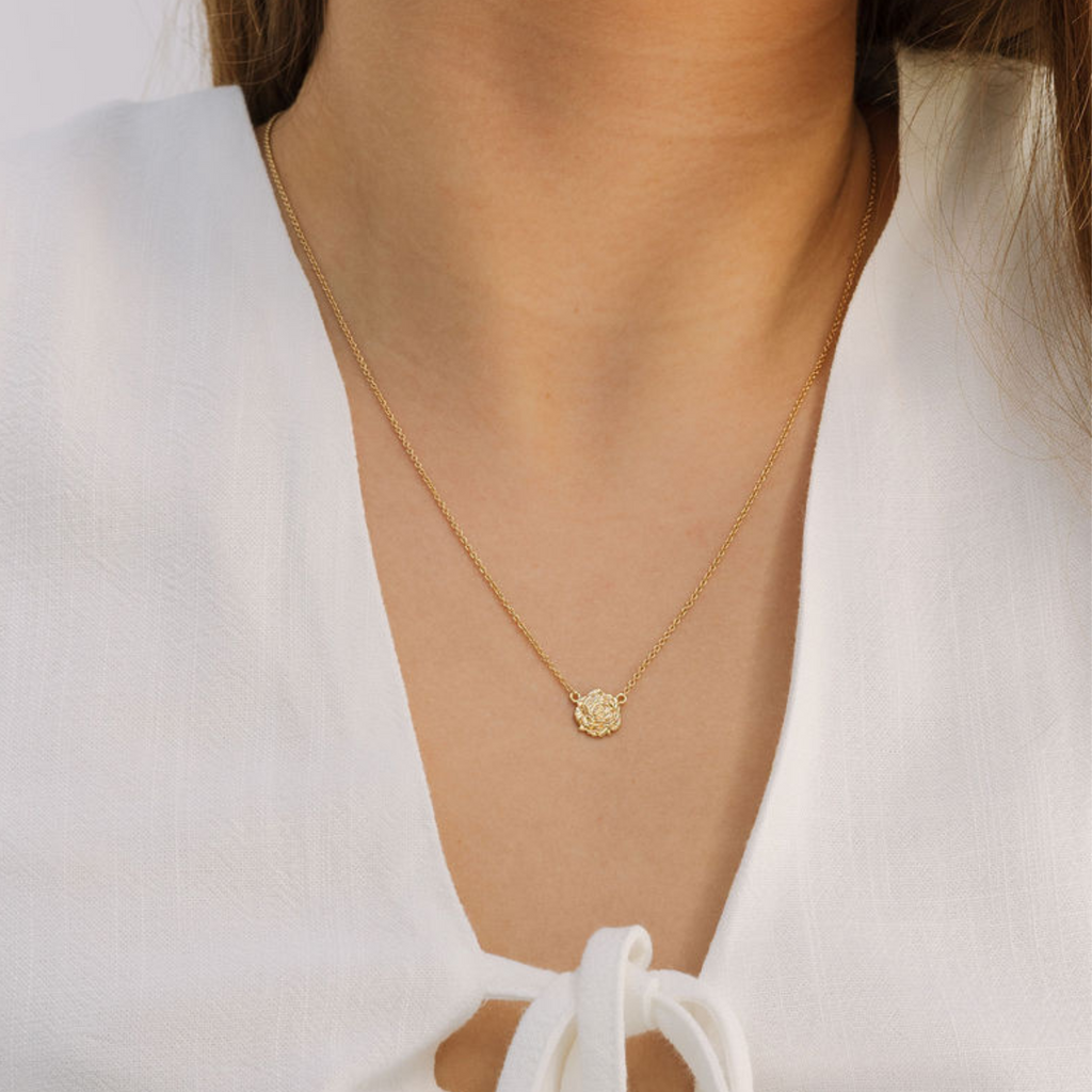 Gold necklace with a small pendant on a person wearing a white top.