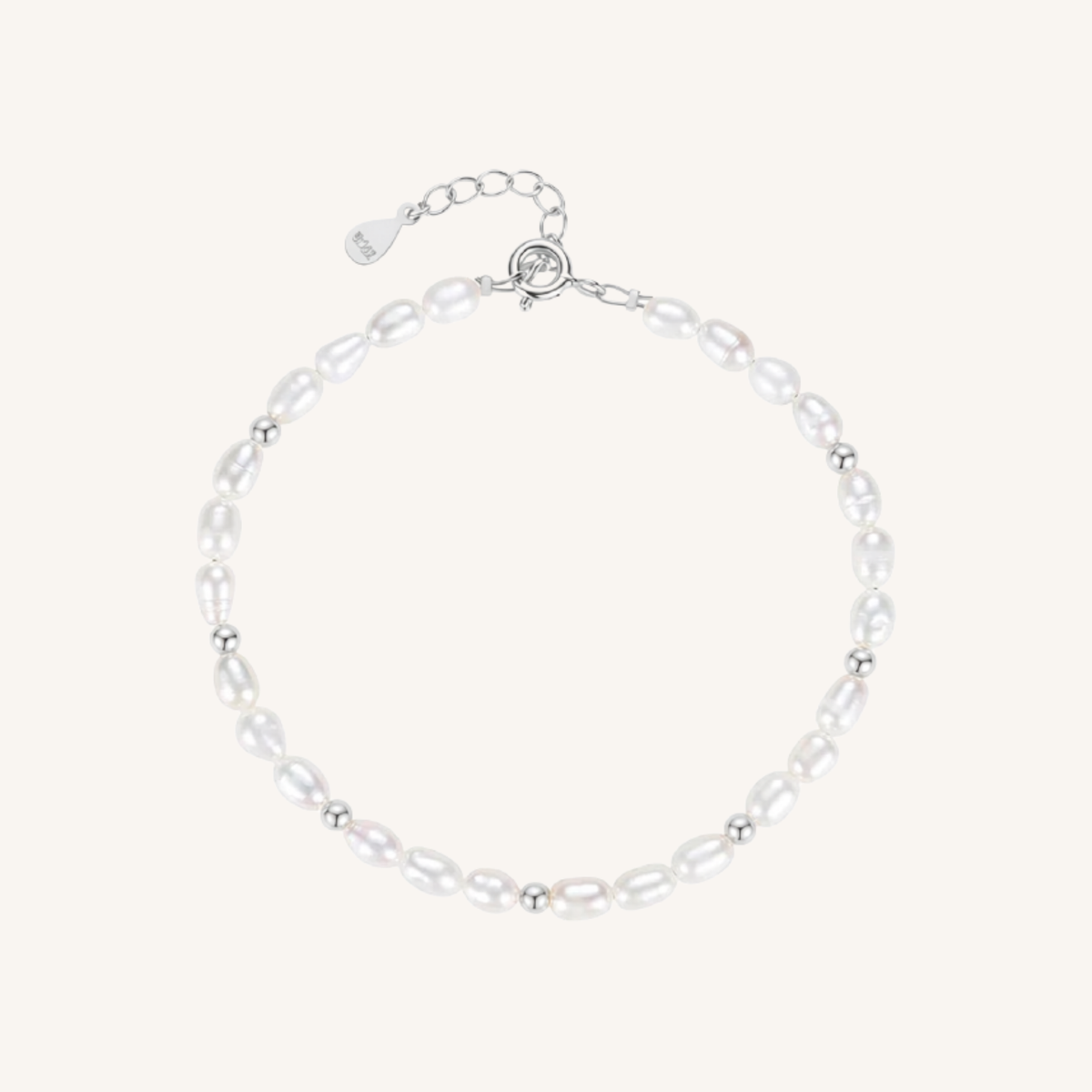 A delicate baroque pearl bracelet with small silver spacer beads and a silver lobster clasp with an extender chain, displayed on a light cream background.