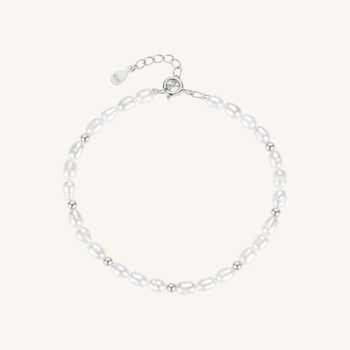 A delicate baroque pearl bracelet with small silver spacer beads and a silver lobster clasp with an extender chain, displayed on a light cream background.