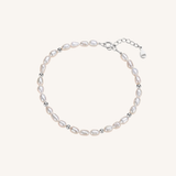 A delicate baroque pearl bracelet with small silver spacer beads and a silver clasp, displayed on a light cream background.