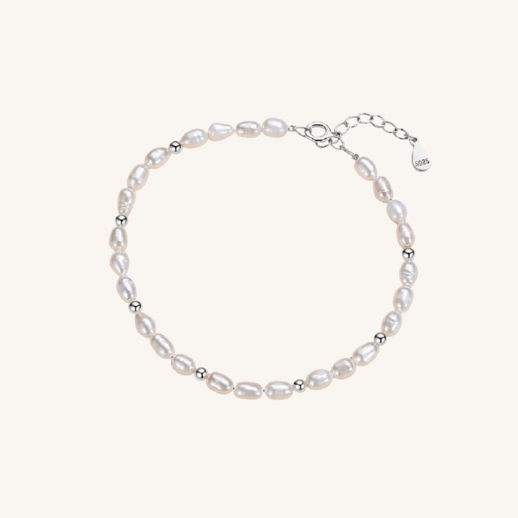 A delicate baroque pearl bracelet with small silver spacer beads and a silver clasp, displayed on a light cream background.