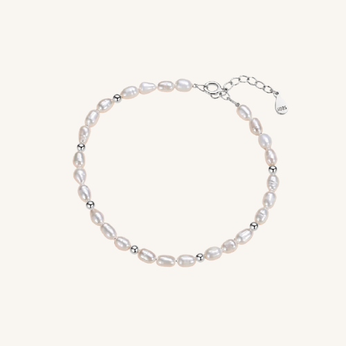 A delicate baroque pearl bracelet with small silver spacer beads and a silver clasp, displayed on a light cream background.