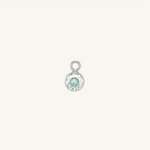 A small round turquoise charm in silver, centered on a light cream background.