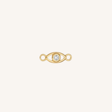 A gold eye-shaped charm with a clear round gemstone in the center, set against a solid off-white background.