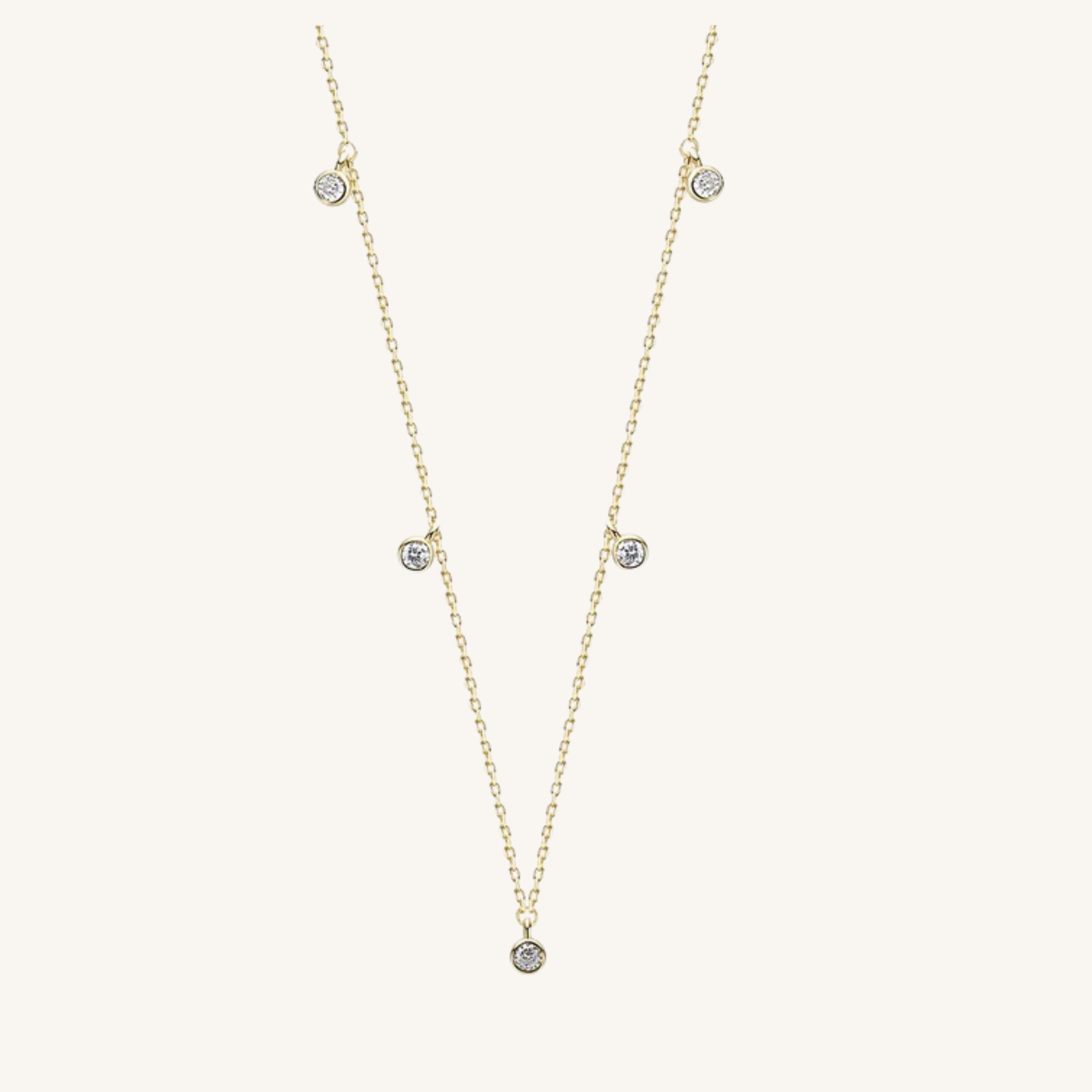 A delicate gold chain necklace featuring five small, round clear gemstones spaced along the chain, displayed on a light cream background.