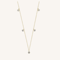 A delicate gold chain necklace featuring five small, round clear gemstones spaced along the chain, displayed on a light cream background.