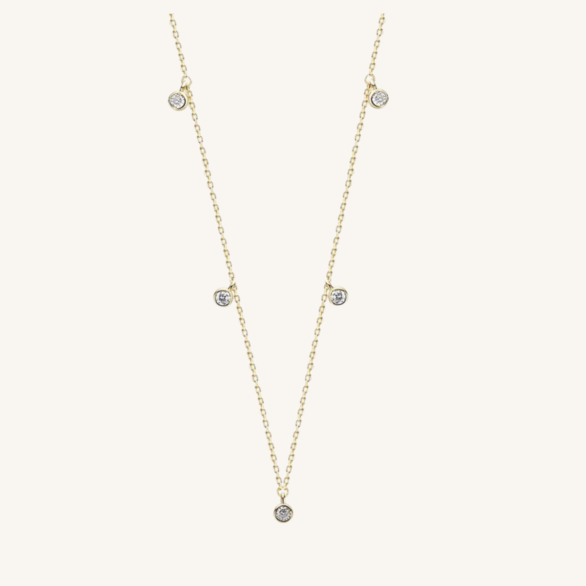 A delicate gold chain necklace featuring five small, round clear gemstones spaced along the chain, displayed on a light cream background.