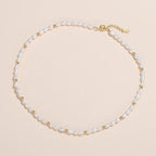 A delicate pearl necklace with small gold spacer beads and a gold clasp, displayed on a light cream background.