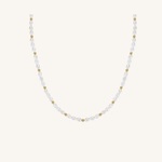 A delicate necklace featuring faceted white pearls and small gold spacer beads, arranged in a U-shape against a solid off-white background.