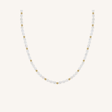 A delicate necklace featuring faceted white pearls and small gold spacer beads, arranged in a U-shape against a solid off-white background.