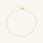 A delicate pearl necklace with small gold spacer beads and a gold clasp, displayed on a light cream background.