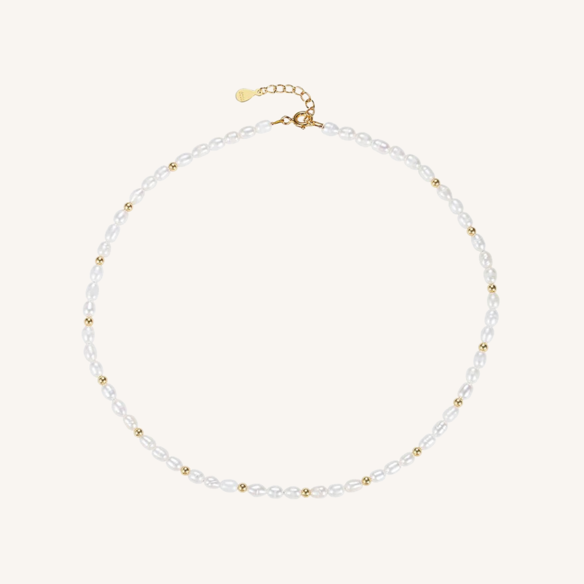 A delicate pearl necklace with small gold spacer beads and a gold clasp, displayed on a light cream background.