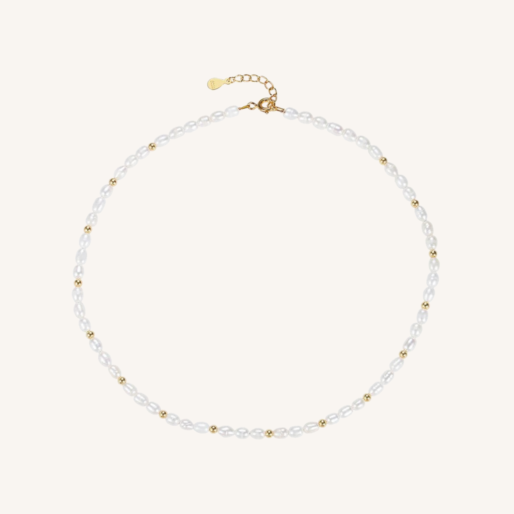 A delicate pearl necklace with small gold spacer beads and a gold clasp, displayed on a light cream background.