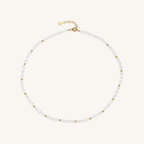 A delicate pearl necklace with small gold spacer beads and a gold clasp, displayed on a light cream background.