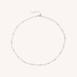 A delicate silver-toned beaded necklace with small, clear faceted beads and a matching silver clasp, displayed on a light cream background.
