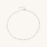 A delicate silver-toned beaded necklace with small, clear faceted beads and a matching silver clasp, displayed on a light cream background.