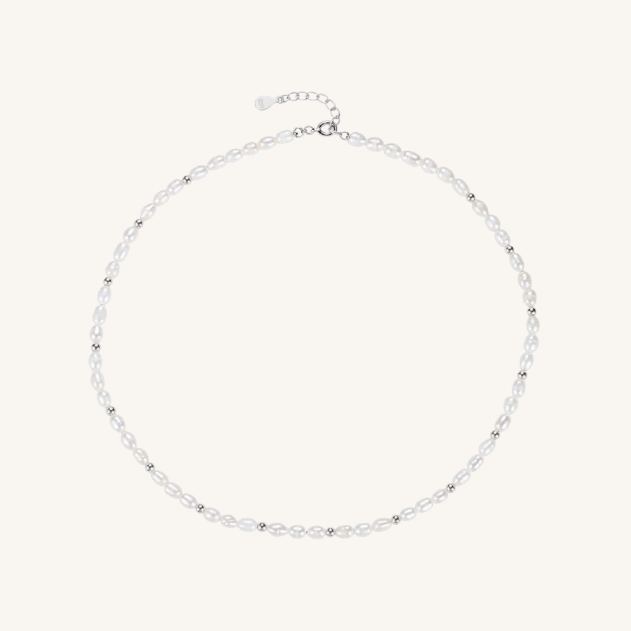 A delicate silver-toned beaded necklace with small, clear faceted beads and a matching silver clasp, displayed on a light cream background.