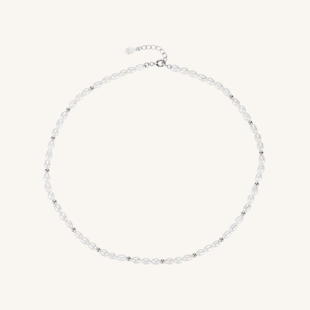 A delicate silver-toned beaded necklace with small, clear faceted beads and a matching silver clasp, displayed on a light cream background.
