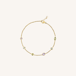 A delicate gold chain bracelet with five small oval and round stones in pastel shades of green, lavender, and light blue, displayed on a clean off-white background.