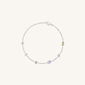 A delicate silver chain bracelet with five small, colorful gemstone accents in purple, green, and clear, displayed on a light cream background.