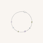 A delicate silver chain bracelet with five small, colorful gemstone accents in purple, green, and clear, displayed on a light cream background.