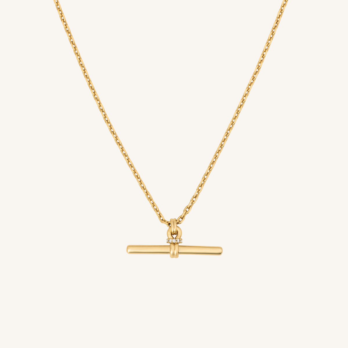 A delicate gold chain necklace featuring a horizontal bar pendant with a small clear gemstone accent at its center, displayed against a solid off-white background.