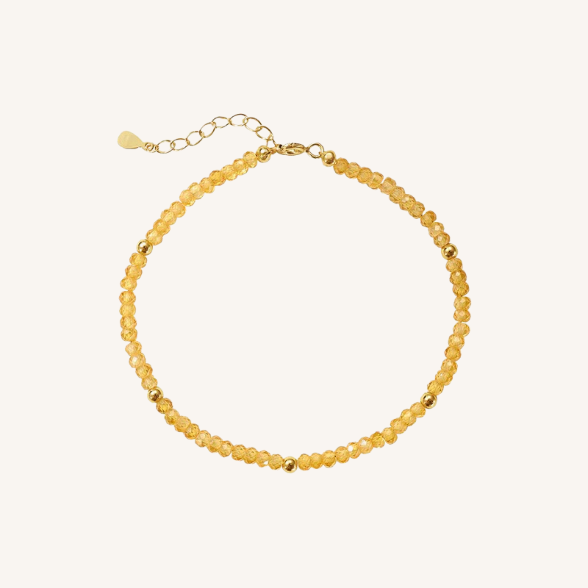A delicate beaded necklace made of small, faceted translucent yellow beads with gold spacer beads and a gold clasp with an extender chain, shown on a light cream background.