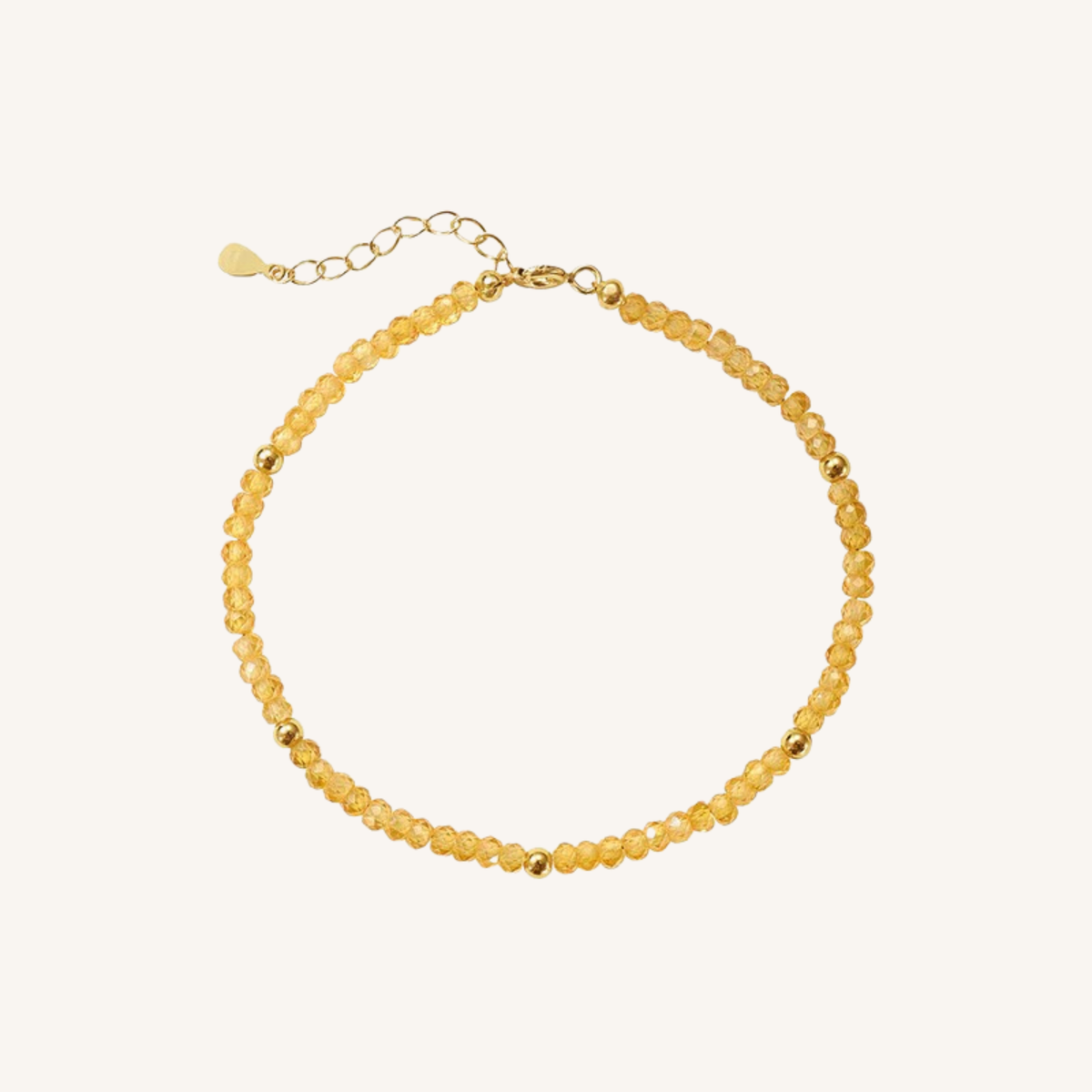 A delicate beaded necklace made of small, faceted translucent yellow beads with gold spacer beads and a gold clasp with an extender chain, shown on a light cream background.