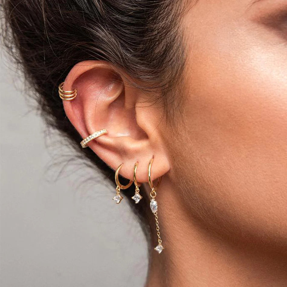 Model wearing a pair of gold dangle earrings with clear gemstones, displayed on a clean off-white background.