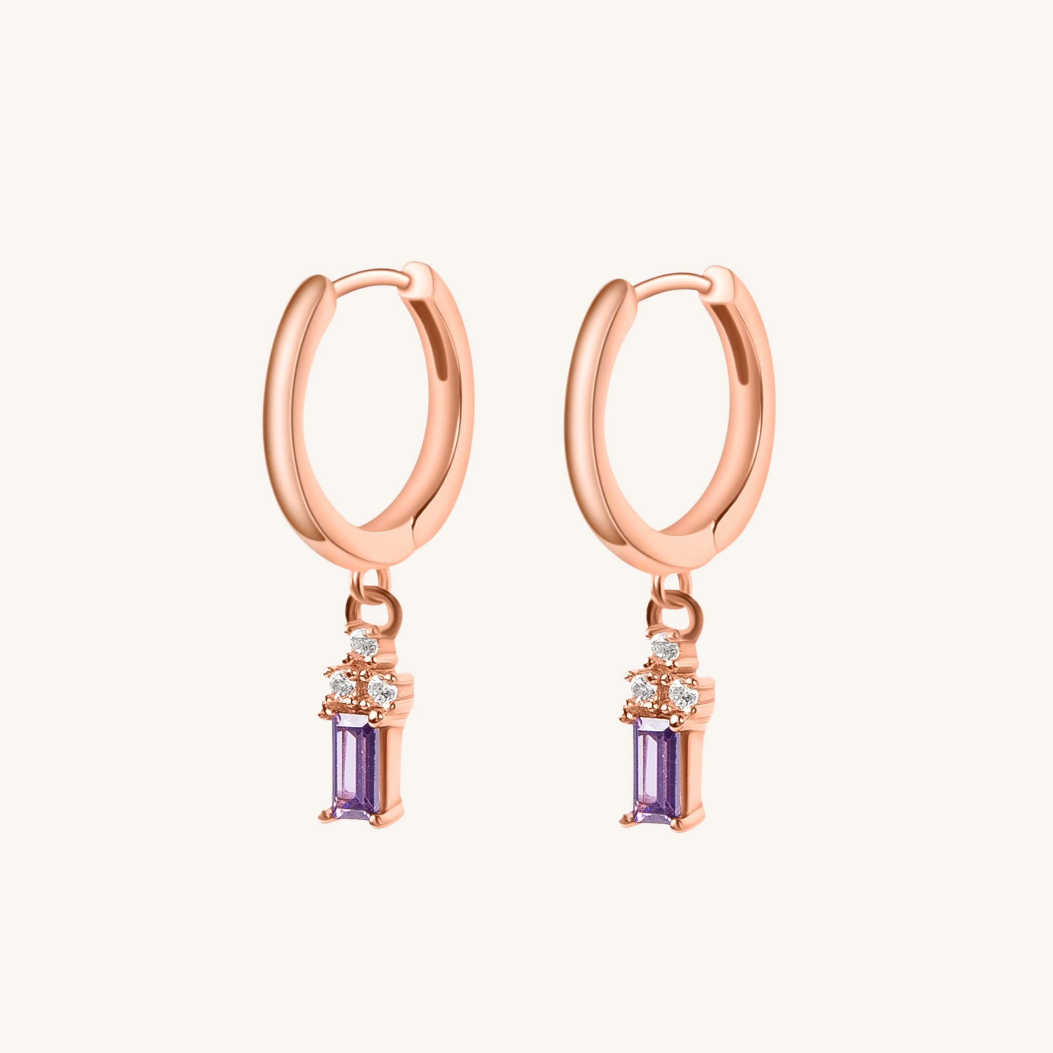 A pair of rose gold hoop earrings with a dangling purple amethyst and small clear cubic zirconia accents, shown on a light cream background.