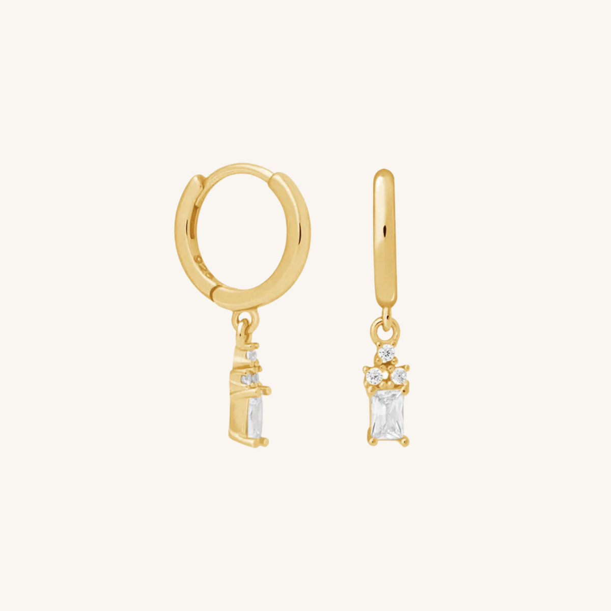 A pair of gold huggie hoop earrings with dangling clear rectangular gemstone charms, displayed on a clean off-white background.