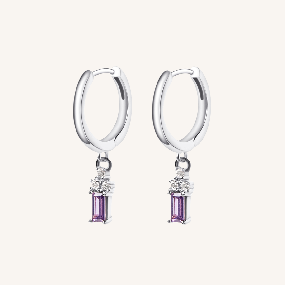 A pair of silver huggie hoop earrings with a dangling rectangular purple gemstone and small clear accent stones, shown on a light cream background.