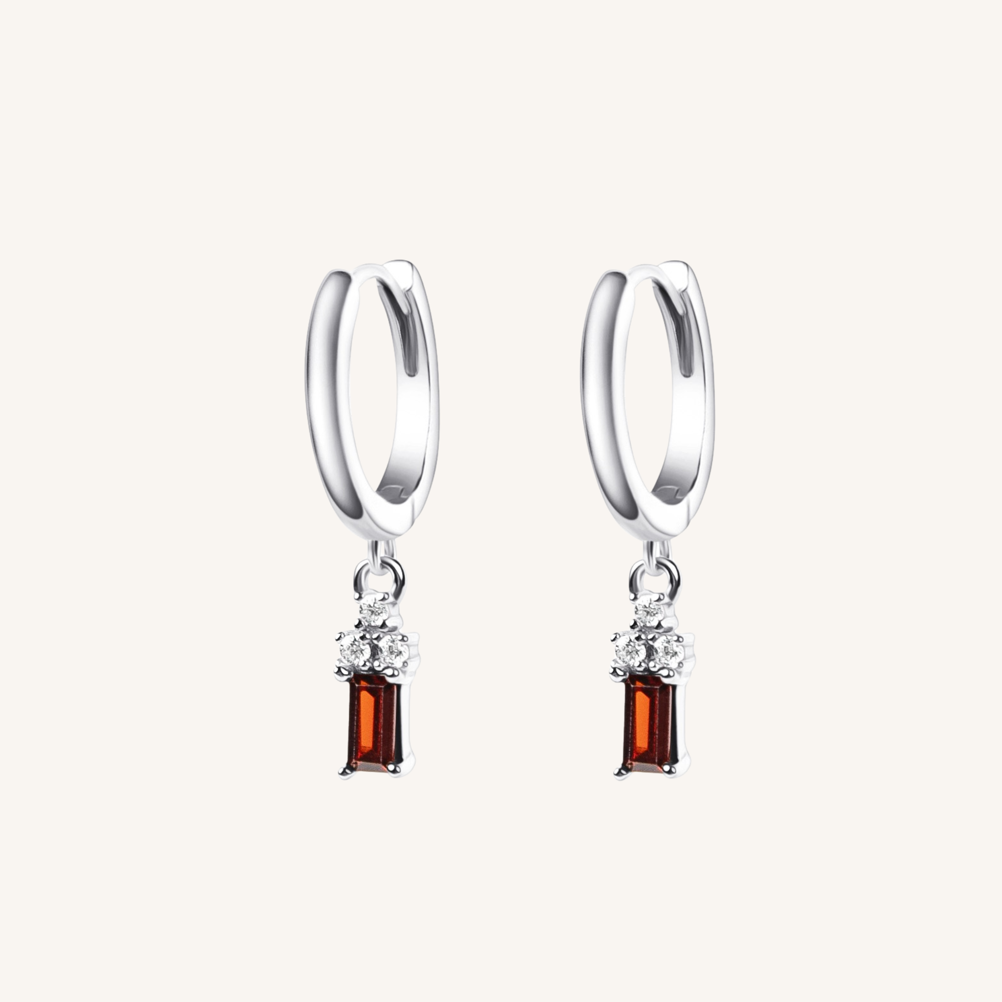 A pair of silver huggie hoop earrings with a dangling rectangular amber gemstone and small clear accent stones, shown on a light cream background.