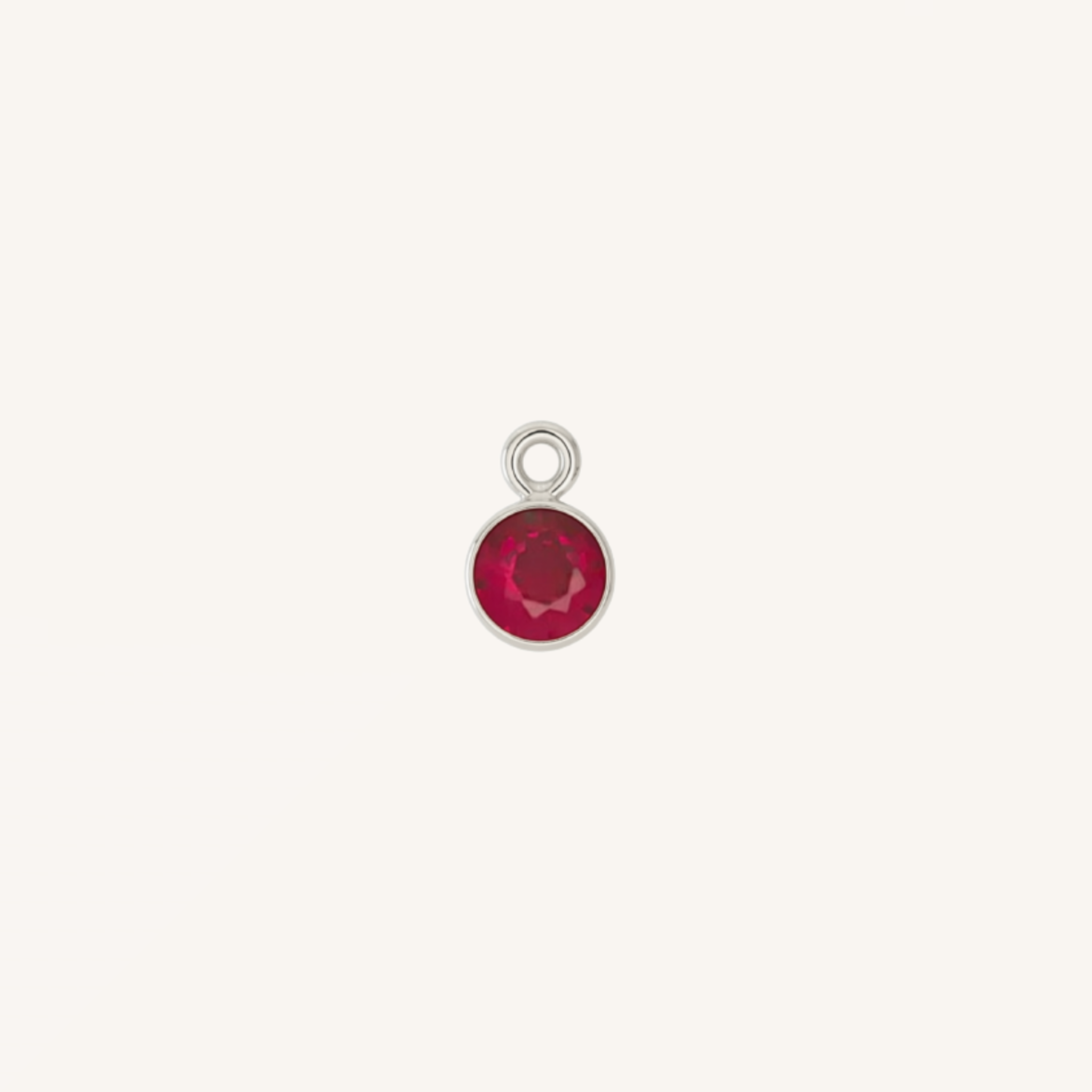 A small round ruby charm in silver, centered on a light cream background.