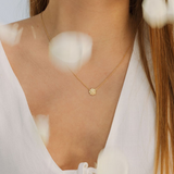 Gold necklace with a round pendant worn by a person against a blurred white background