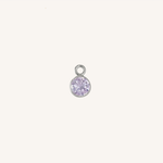 A small round alexandrite charm in silver, centered on a light cream background.